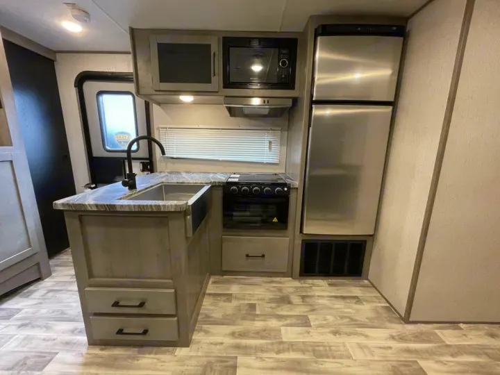 Modern RV rental kitchen interior: stainless steel refrigerator, microwave, stove, island sink, and wood-look floor.. Keystone Kodiak 2022