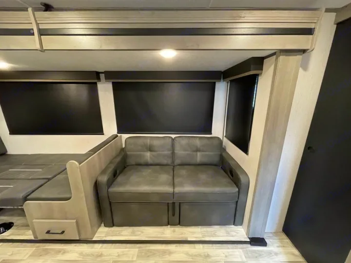 RV rental interior features a grey sofa, convertible dinette/bed, black window shades, and light wood accents.. Keystone Kodiak 2022