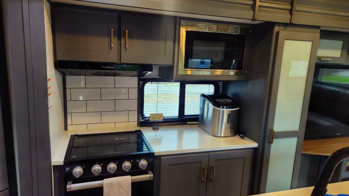 RV rental kitchen: modern gray cabinets, white counters, stove, microwave, ice maker, and subway tile backsplash.. Keystone RV Bullet Premier Ultra Lite 2022