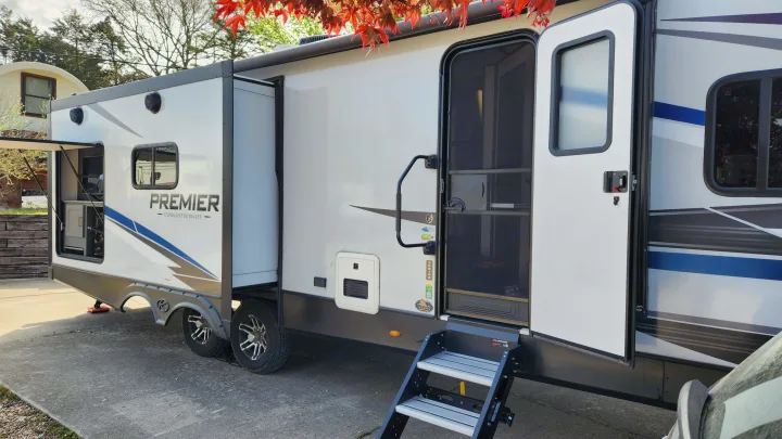 A white Premier Ultra Lite by Bullet RV rental is parked with its steps down and slide-out extended, ready for outdoor adventures.. Keystone RV Bullet Premier Ultra Lite 2022