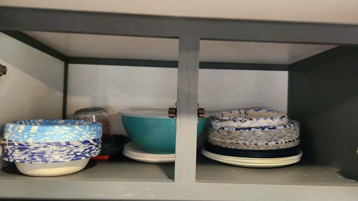 RV rental: Inside a compact cabinet, organized stacks of blue/white paper plates, white plastic plates, and a large turquoise bowl.. Keystone RV Bullet Premier Ultra Lite 2022