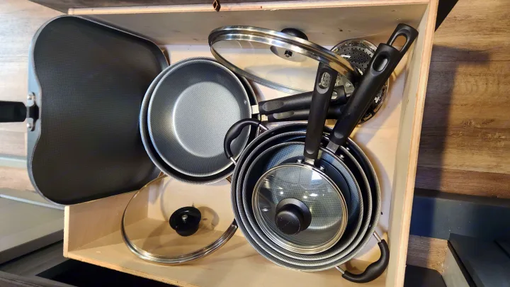 Inside an RV rental drawer: compact, nested pots, pans, and lids are neatly stored, showing efficient kitchen organization for travel.. Keystone RV Bullet Premier Ultra Lite 2022