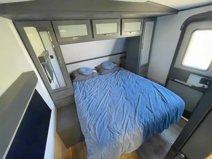 An RV rental bedroom features a blue bed, ample dark wood storage, and a mirrored wardrobe for comfortable stays.. Keystone RV Bullet Premier Ultra Lite 2022