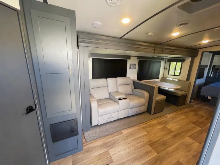 Clean RV rental interior with gray cabinetry, a light reclining loveseat, and a dinette area with wood-look flooring.. Keystone RV Bullet Premier Ultra Lite 2022