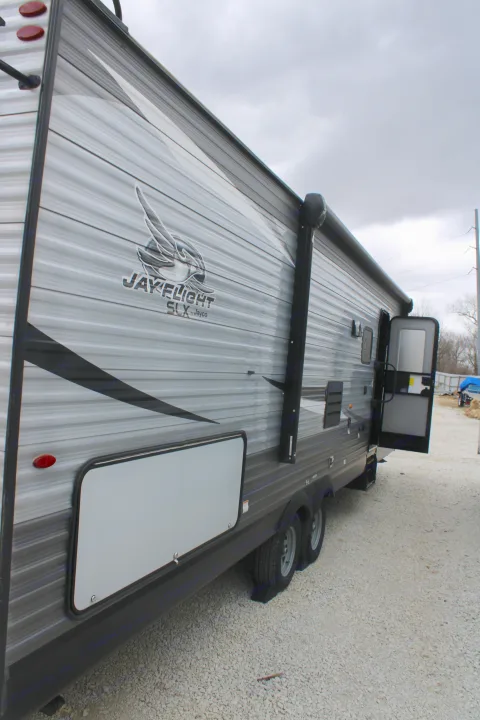 Side view of a grey Jayco Jay Flight RV rental trailer, featuring an open door and storage compartment on gravel.. Jayco Jayflight SLX 8 2021