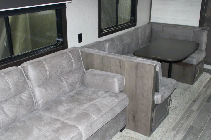 Comfortable gray sofa and U-shaped dinette with a table, ideal for seating and dining inside an RV rental.. Jayco Jayflight SLX 8 2021