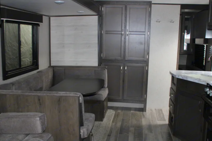 View of an RV rental's cozy dinette with grey seating and a dark table, next to dark wood-look cabinets and kitchen counter.. Jayco Jayflight SLX 8 2021