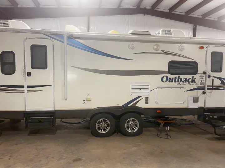 This white Outback Keystone Super-Lite travel trailer, perfect for an rv rental, shows its side with doors, awning, and roof AC units.. Keystone RV Outback Toy Hauler 2013