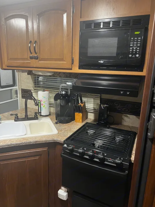 An rv rental kitchen with wood cabinets, microwave, stove, sink, Keurig, and a gas safety alarm for comfortable travel.. Keystone RV Outback Toy Hauler 2013