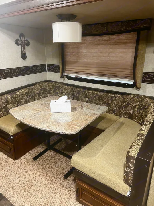 Cozy RV rental dinette with U-shaped booth seating, patterned backrests, and a stone-look table under a ceiling light.. Keystone RV Outback Toy Hauler 2013