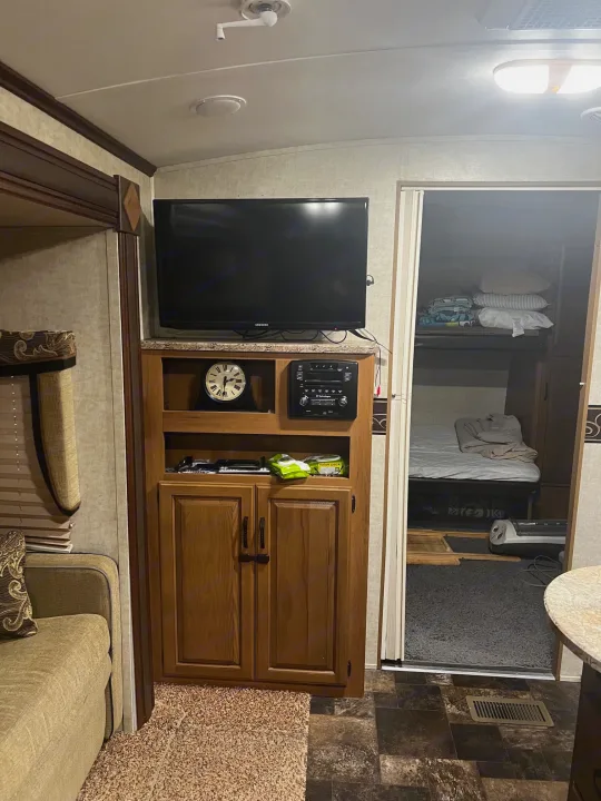 Cozy RV rental interior showing living area with TV, storage, and a bunk bed area, perfect for travel comfort.. Keystone RV Outback Toy Hauler 2013