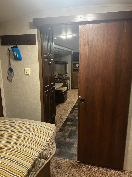 RV rental interior: Bedroom with striped bed, opening to living area via a partially open wooden sliding door.. Keystone RV Outback Toy Hauler 2013