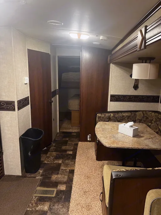 RV rental interior showing a small dining area with a patterned booth, a table, and visible bunk beds beyond.. Keystone RV Outback Toy Hauler 2013