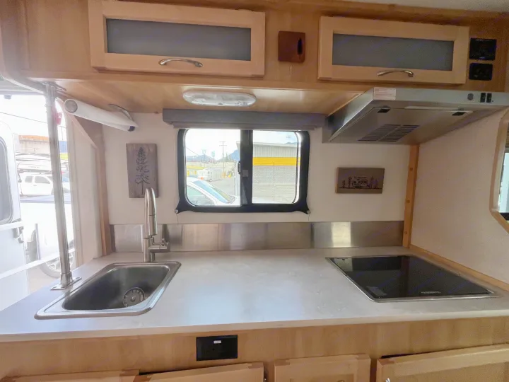 Inside an RV rental: a modern kitchen with a stainless steel sink, flat-top stove, wood cabinets, and outside view.. Escape Trailer Escape Trailer Trailer 2022