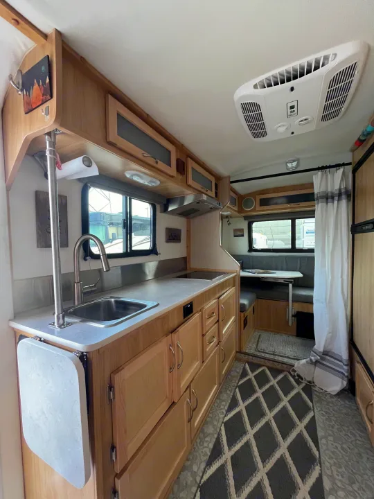 Bright RV rental interior: well-lit kitchen with sink, light wood cabinets, dining booth, and patterned rug.. Escape Trailer Escape Trailer Trailer 2022