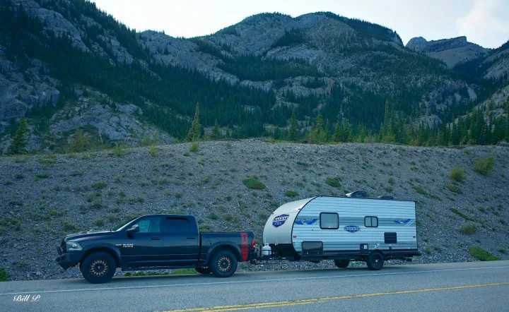Exploring nature with an RV rental. A truck tows a camper on a mountain road, surrounded by rocky peaks.. Forest River Salem 2022