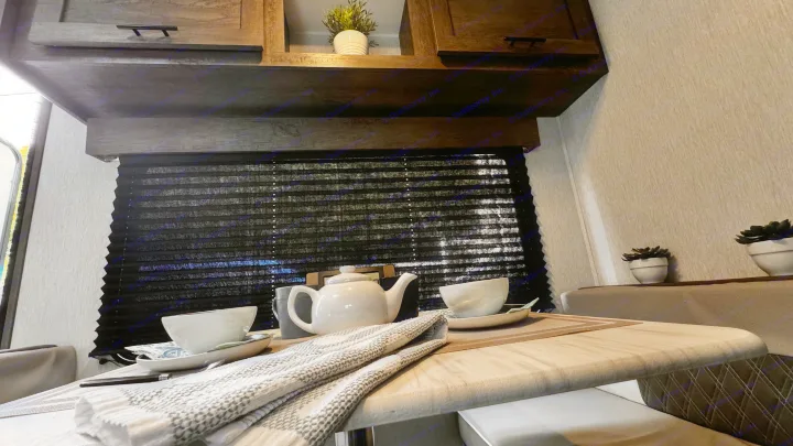 Cozy RV rental dining area with a white tea set on the table, overhead cabinets, and black pleated blinds.. Forest River Salem 2022