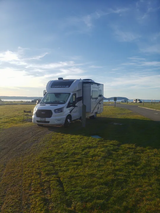 White Compass AWD RV rental parked at a scenic waterfront campground with extended slide-out, ready for adventure.. Thor Compass 2024