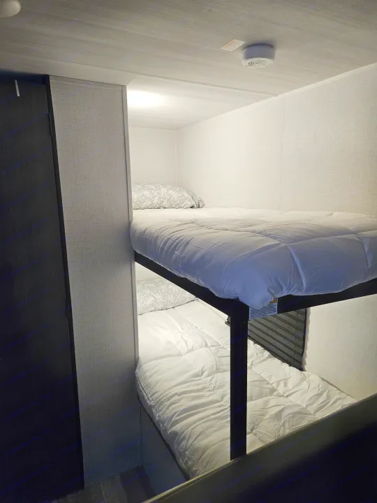 An RV rental's clever use of space: two stacked bunk beds, with clean white bedding, a pillow, and a ceiling smoke alarm.. Keystone RV Keystone Hideout 175BH 2024