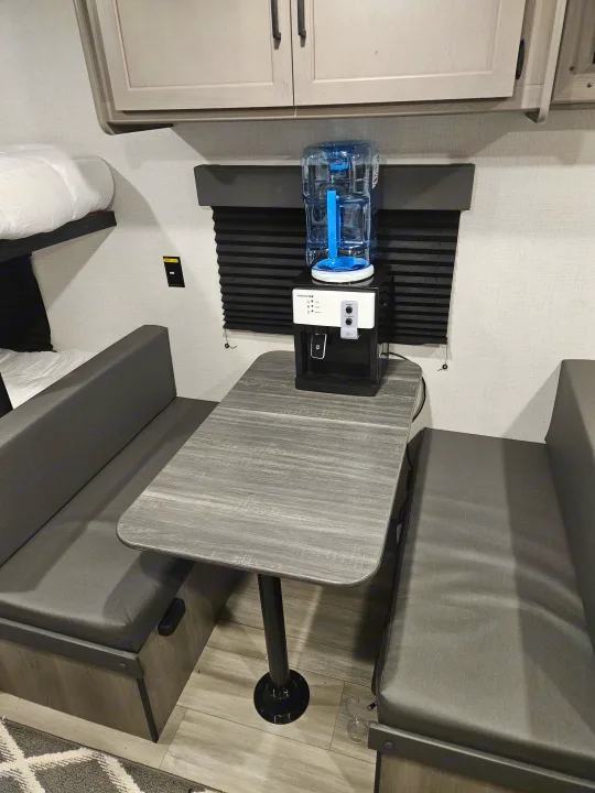 This RV rental interior features a compact dinette with a water dispenser, cozy bunk beds, and storage cabinets.. Keystone RV Keystone Hideout 175BH 2024