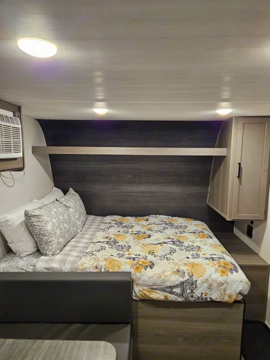 Cozy RV rental bedroom with floral quilt, dark wood accents, and an AC unit for comfortable travels.. Keystone RV Keystone Hideout 175BH 2024