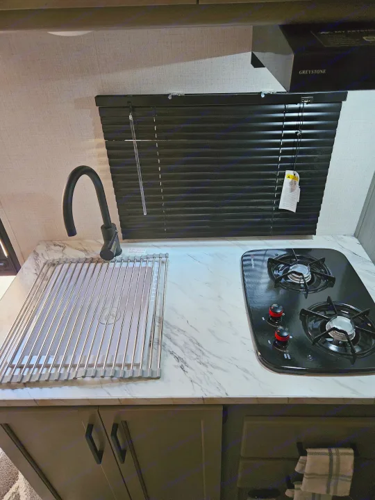 Compact RV rental kitchen featuring a sink with a roll-up dish rack, a two-burner cooktop, and marble-look counters.. Keystone RV Keystone Hideout 175BH 2024