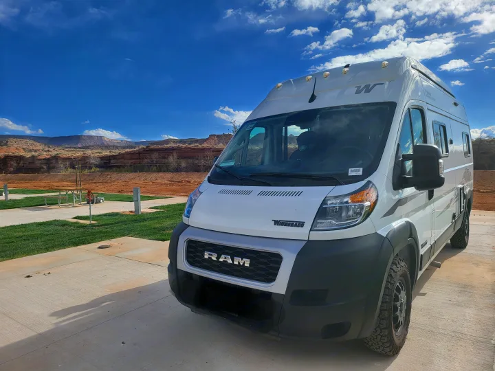 White Winnebago rv rental camper van at a scenic desert campground, featuring red rock mountains under a bright blue sky.. Winnebago Solis 2024