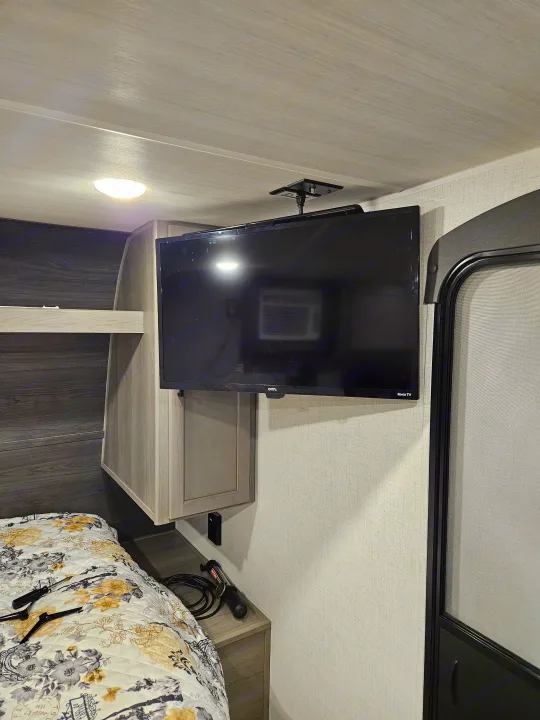 Compact RV rental bedroom featuring a ceiling-mounted TV, bed with floral comforter, and built-in storage.. Keystone RV Keystone Hideout 175BH 2024