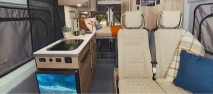 An RV rental interior featuring a compact kitchen, elevated bed, and two front passenger seats, offering comfort for travel.. Winnebago Solis 2024