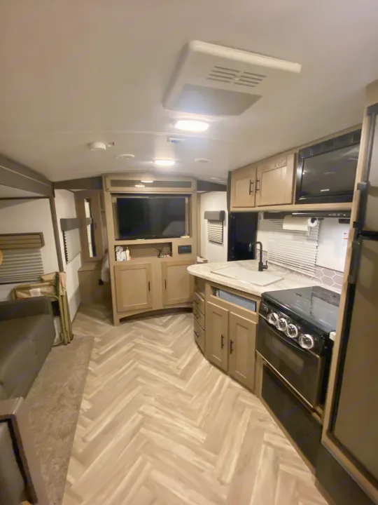 Clean RV rental interior: modern kitchen, living space with TV & couch, herringbone floor.. Cruiser RV Shadow Cruiser 2021