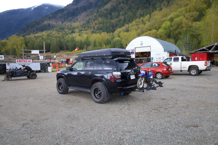 Black 4Runner with iKamper rooftop tent and dirt bike, parked at a mountain vehicle rental office, ideal for RV rental adventures.. Toyota Other 2015