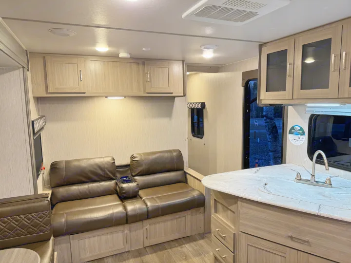 RV rental interior featuring a modern living space with light wood cabinets, comfortable brown leather seating, and a kitchen area.. Coachmen Freedom Express 2020
