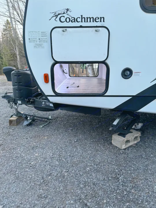 Coachmen RV rental with open storage, hitch, and stabilizer jacks on gravel, set for travel.. Coachmen Freedom Express 2020