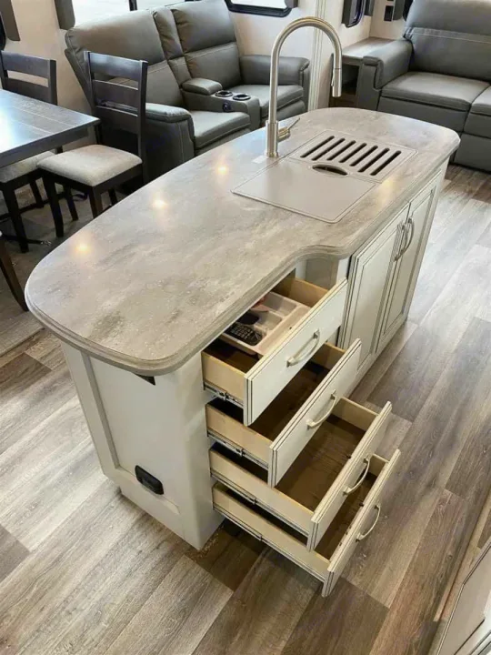 Modern RV rental kitchen island with sink and open drawers revealing organized storage, showcasing compact, functional design.. Keystone Cougar 2022