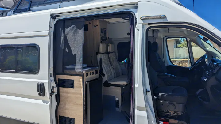 This white RV rental showcases its open side door, revealing a modern interior with a kitchen, seating, and the front cabin.. Winnebago Solis 59PX 2023