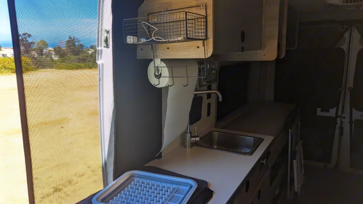 RV rental interior: Kitchenette with sink, paper towels, drying rack, and a bright screened window view.. Winnebago Solis 59PX 2023
