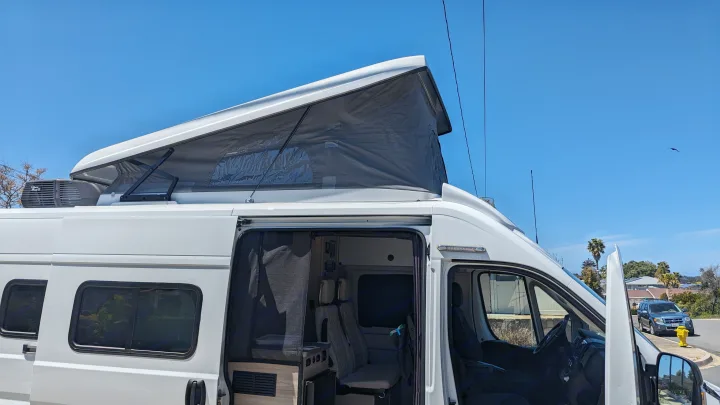 White camper van RV rental with pop-top roof extended. Side door open, revealing interior. Perfect for outdoor adventure.. Winnebago Solis 59PX 2023