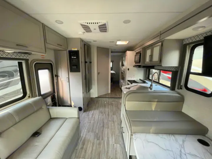 Spacious and modern RV rental interior featuring a comfortable living area, full kitchen, and dining booth.. Thor Coleman 2023