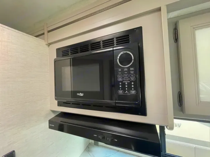 Compact RV rental kitchen with a black microwave and range hood. Ready for your travel meals.. Thor Coleman 2023