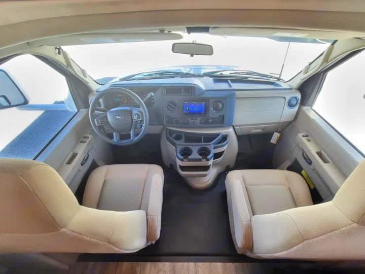 RV rental's front cabin: driver's steering wheel, dashboard with screen, and two cream seats, seen from behind.. Thor Coleman 2023