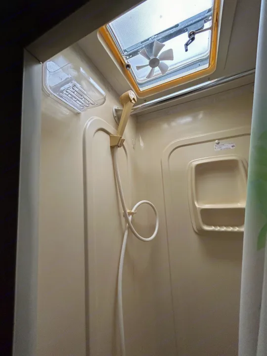Inside an RV rental shower: a beige stall with a ceiling vent/fan, handheld shower, soap dish, and a curtain.. Coachmen Catalina 2003