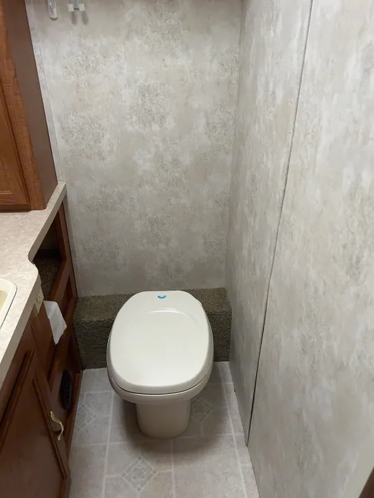 Clean RV rental bathroom featuring a white toilet, tiled floor, and light patterned walls with a wood vanity.. Coachmen Catalina 2003