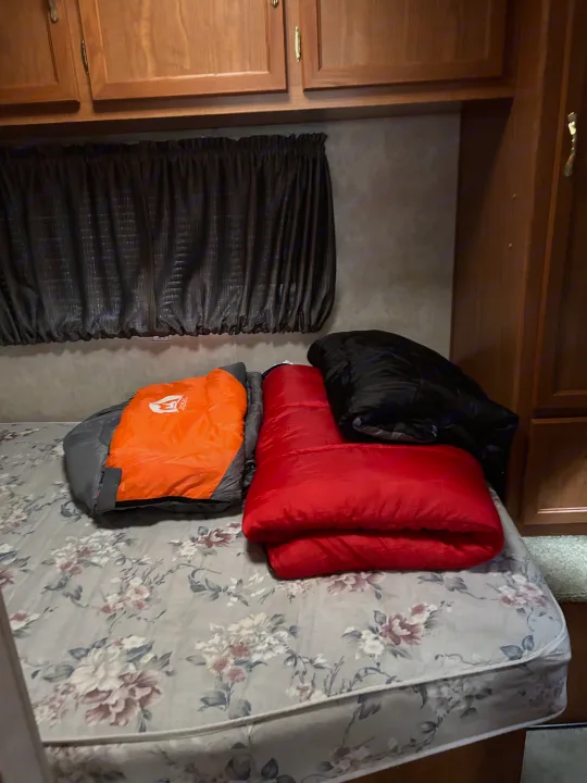 An RV rental bedroom with three colorful sleeping bags (orange, red, black) on a floral mattress.. Coachmen Catalina 2003