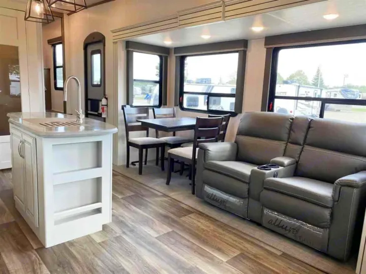Inside a spacious RV rental: modern kitchen island, dining table, and comfy reclining sofa in a light-filled living area.. Keystone Cougar 2022