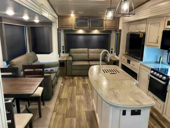 This spacious RV rental interior features a modern kitchen island with sink, a cozy living area, dining table, and wood flooring.. Keystone Cougar 2022