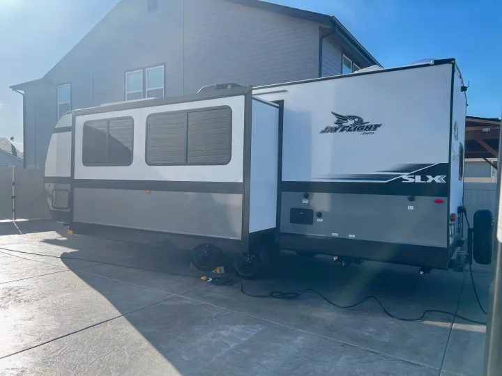 This Jayco travel trailer, available for RV rental, is parked outside a home with its slide-out extended.. Jayco Jayflight 2024