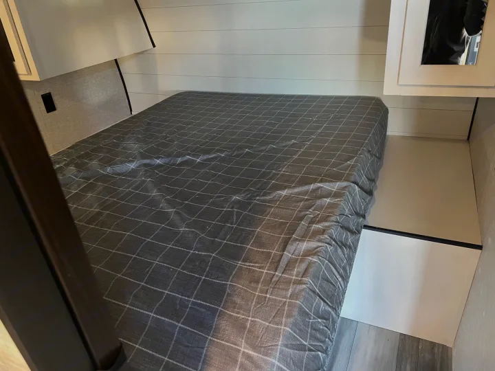 Cozy RV rental bedroom featuring a plaid-covered bed, white shiplap walls, and compact storage with a mirror.. Jayco Jayflight 2024