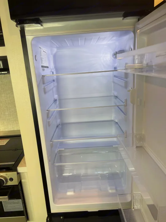 An empty, brightly lit RV rental refrigerator, showcasing its adjustable shelves and clear bins, ready for use.. Jayco Jayflight 2024
