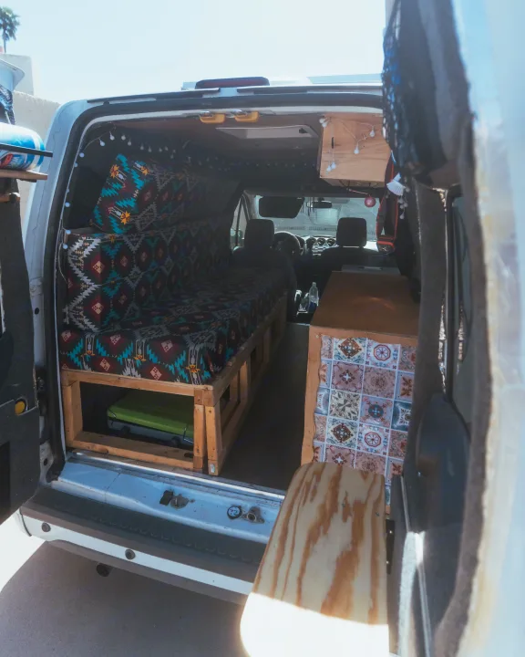 Inside this customized RV rental campervan, see the bed with patterned cushions, wooden structures, and a tiled cabinet.. Ford Transit 2011