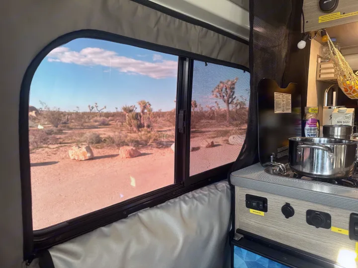 RV rental interior with a desert view of Joshua trees, featuring a compact kitchen with a pot and supplies.. Winnebago Solis 2023